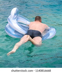 A Fat Man Is Floating On An Inflatable Circle In The Pool