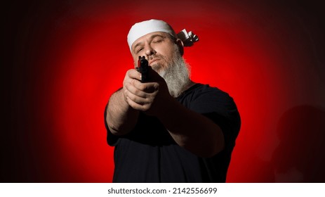 A Fat Man With A Gray Beard And A Bandage On His Head Aims With A Gun On A Dark Background