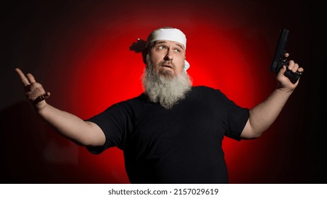 A Fat Man With A Gray Beard And A Bandage On His Head Holds A Gun In His Hand And Points His Finger To The Side On A Dark Background