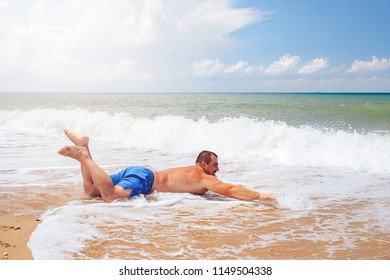  Fat Man On The Sea Coast Pretends To Be Floating Lying On The Sand. Toned.