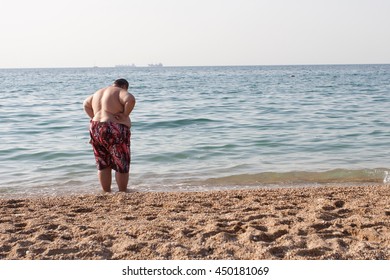 A Fat Man In Red Shorts Stands On The Shore Of The Sea