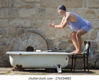 Fat man in retro swimsuit jumps to the outdoor bathtub. Funny swimmer in vintage style and bathing cap starts to swim in the tub. Home vacations. Domestic holiday.