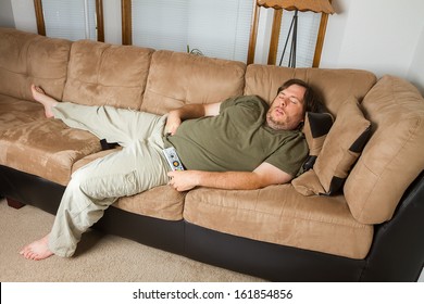 Fat man sleeping on the couch with his hand down his pants