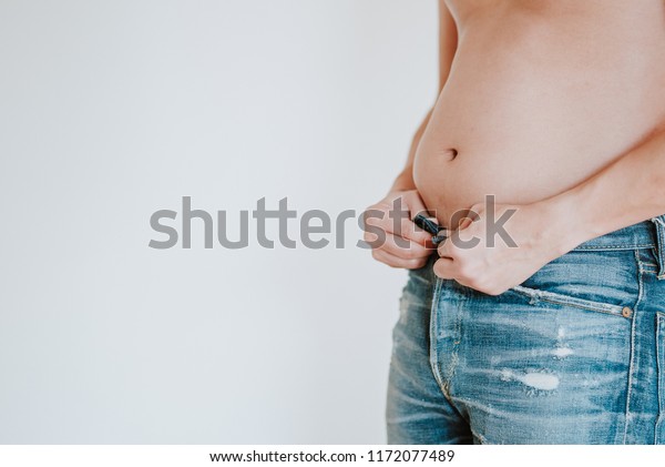 太った男がジーンズのズボンのボタンを下ろそうとして 太った腹が出たので立ち往生し 太り過ぎの体脂肪 白い背景にフィットネスとダイエットのコンセプトを調べる の写真素材 今すぐ編集