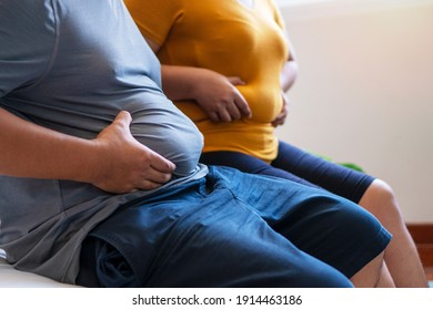 Fat man and woman holding their big belly waistline sitting on the bed suffering from extra weight. Couple heavy body size worry problem bad healthy in the bedroom.Overweight loss unhealthy concept.