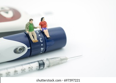 Fat man and woman miniature figure sitting on lancet with syringe for insulin and Glucose meter for check blood sugar level using as Medicine, diabetes, glycemia, health care and people concept.