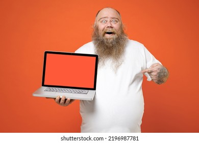 Fat Pudge Obese Chubby Overweight Tattooed Bearded Big Belly Man In White T-shirt Point Index Finger On Laptop Pc Computer Blank Screen Workspace Area Isolated On Red Orange Background Studio Portrait