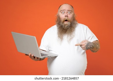 Fat Shock Pudge Obese Chubby Overweight Tattooed Blue-eyed Bearded Man 30s Has Big Belly Wear White T-shirt Point Inedx Finger On Laptop Pc Computer Isolated On Red Orange Background Studio Portrait.