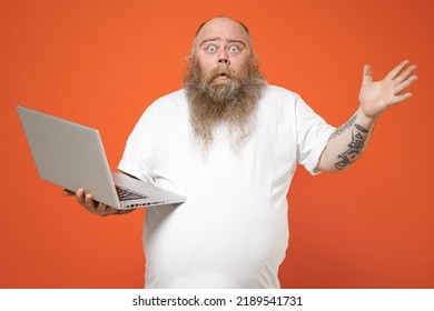 Fat Shocked Pudge Obese Chubby Overweight Tattooed Blue-eyed Bearded Man 30s Has Big Belly Wear White T-shirt Hold Laptop Pc Computer Spread Hands Isolated On Red Orange Background Studio Portrait.