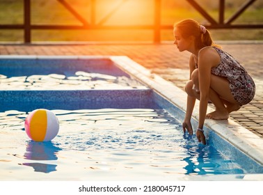 Fat Tanned Happy Girl With Dark Hair Braided In Bun In Bright Summer Suit Is Playing Near Pool With Inflatable Ball, Against The Background Of Golden Summer Evening Sun