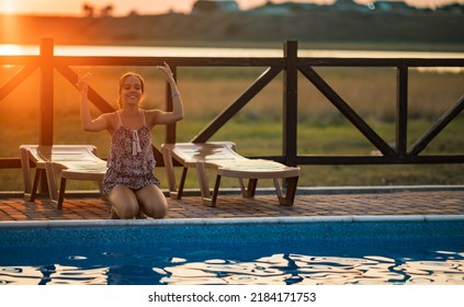 Fat Tanned Happy Girl With Dark Hair Braided In Bun In Bright Summer Suit Is Playing Near Pool With Inflatable Ball, Against The Background Of Golden Summer Evening Sun