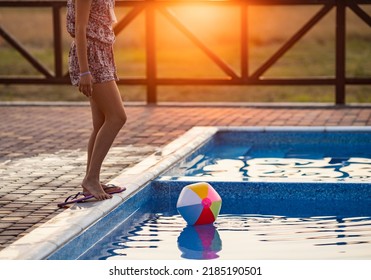 Fat Tanned Happy Girl With Dark Hair Braided In Bun In Bright Summer Suit Is Playing Near Pool With Inflatable Ball, Against The Background Of Golden Summer Evening Sun