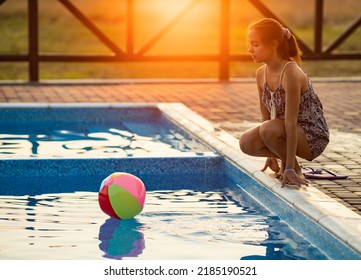 Fat Tanned Happy Girl With Dark Hair Braided In Bun In Bright Summer Suit Is Playing Near Pool With Inflatable Ball, Against The Background Of Golden Summer Evening Sun