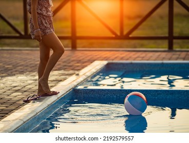 Fat Tanned Happy Girl With Dark Hair Braided In Bun In Bright Summer Suit Is Playing Near Pool With Inflatable Ball, Against The Background Of Golden Summer Evening Sun