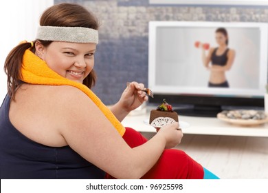 Fat woman choosing chocolate cake instead of doing gymnastics, smiling happily.?
