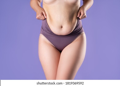 Fat woman in corrective panties, flabby belly after pregnancy, overweight female body on purple background, studio shot