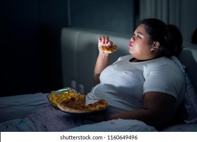 Fat woman eating pizza on bed while watching movie before sleep