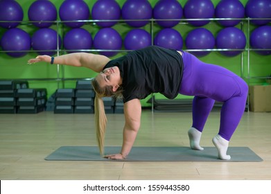 Fat Woman Is Engaged In Pilates In A Fitness Gym. A Girl With A Lot Of Overweight Trying To Lose Weight With The Help Of Sports And Yoga, Does The Bridge Exercise.