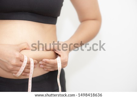 Fat woman hand holding excessive belly fat with measuring tape on white background. Shape up healthy stomach muscle and diet lifestyle to reduce belly concept.