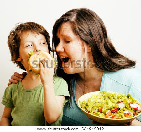 fat woman holding salad and little cute boy with hamburger teasing