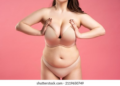 Fat woman with large breasts in a push-up bra on pink background, overweight female body, studio shot