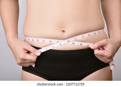 Fat woman measuring her belly fat, Overweight woman check out her obesity, Woman muffin top waistline.