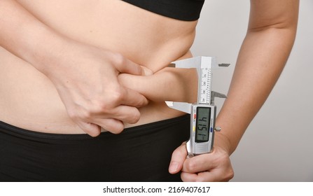 Fat woman measuring her belly fat by vernier caliper scale, Overweight woman check out her obesity, Woman muffin top waistline. - Shutterstock ID 2169407617