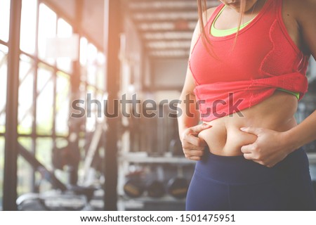 Fat woman, Obese woman hand holding excessive belly fat isolated on gym background, Overweight fatty belly of woman, Woman diet lifestyle concept to reduce belly and shape up healthy stomach muscle.