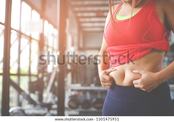 Fat woman, Obese woman hand holding excessive\
belly fat isolated on gym background, Overweight fatty belly of\
woman, Woman diet lifestyle concept to reduce belly and shape up\
healthy stomach muscle.