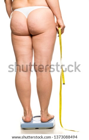 a fat woman stands on a scales and holds a measuring tape on white background
