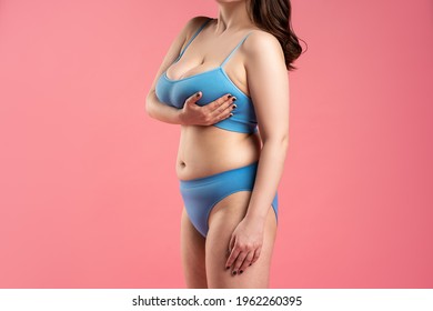 Fat woman with very large breasts in blue underwear on pink background, body care concept, studio shot