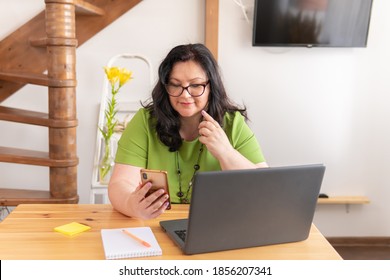 Fat Woman Works With A Laptop At The Table In The Office. She Reads The News.