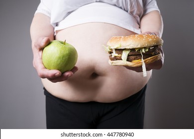 Fat women suffer from obesity with big hamburger and apple in hands, junk food concept on a gray background