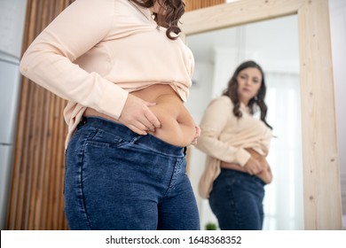 Fat. Young woman in a beige blouse examining her abs