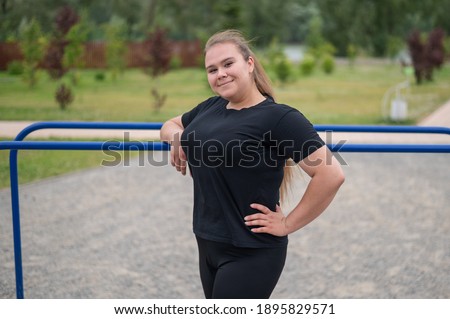 Fat young woman posing by the uneven bars outdoors.