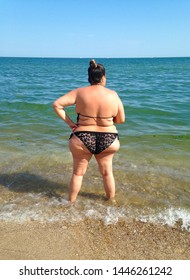 A fat young woman stands on the shore.