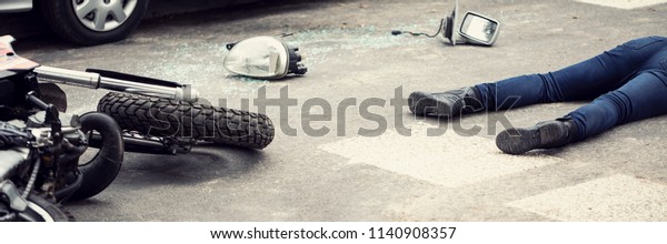 Fatal aftermath of a\
car accident concept - dead body and crashed motorcycle parts lying\
on the road