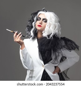 A fatal beauty in a daring fashion image with black and white hair. A rebellious stylish image for Halloween. a young woman in a black and white outfit smokes a cigarette using a mouthpiece