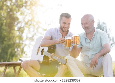 Father and adult son toasting beer mugs and playing guitar outdoors - Powered by Shutterstock