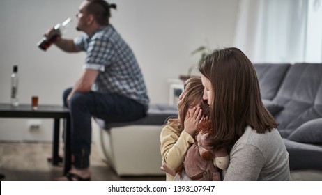 The Father Is An Alcoholic Drinks Alcohol From A Bottle. The Child Is Closed From The Problem Of Drunkenness In The Family. Mother Comforting Daughter From Drinking. Difficulties In The Family.