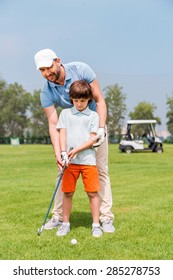 Father is always near to help me. Joyful young manteaching his son to play golf while standing on the golf course