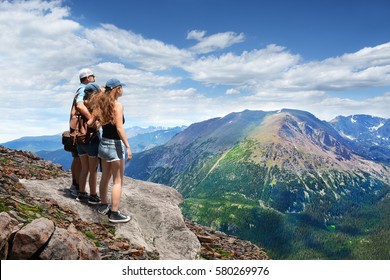 Father with arms around his family looking at summer mountains landscape, on hiking trip, on  top of  mountain. View from Trail Ridge Road. Estes Park, Rocky Mountains National Park, Colorado. 