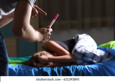 Father Asking For Explanation Showing Pregnancy Test To A Sad Pregnant Teen Who Is Lamenting Lying On The Bed In Her Room