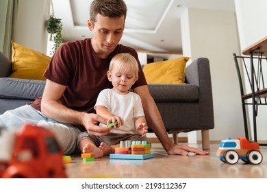 Father assisting his baby boy playing sorter sitting on floor in living-room with sofa on background, surrounded with car toys, waiting mom to come home from work. Education toys, child development - Powered by Shutterstock