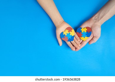 Vater und autistischer Sohn Hände, die Puzzle Puzzle-Herzform hält. Konzept zur Unterstützung der Familie bei Störungen des Autismus-Spektrums. Tag des Autismus-Bewusstseins