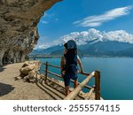 Father with baby carrier looking at lakeside town Nago Torbole seen from hiking trail Sentiero del Ponale at Garda Lake, Trentino, Northern Italy. Surrounded by mountains of Garda Hills. Family trip