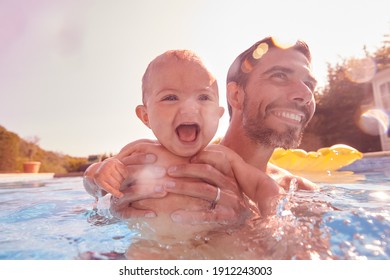 Father With Baby Daughter Having Fun On Summer Vacation Splashing In Outdoor Swimming Pool