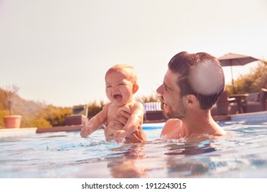 Father With Baby Daughter Having Fun On Summer Vacation Splashing In Outdoor Swimming Pool