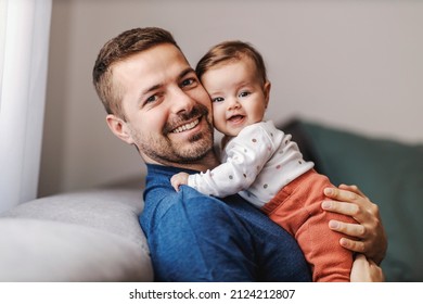 Father and baby girl hugging and smiling at the camera while sitting on the sofa. - Powered by Shutterstock