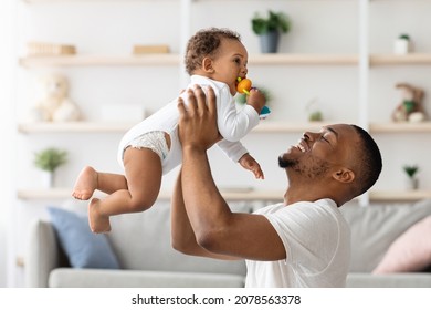 Father Baby Relationship. Happy Black Man Lifting Up His Adorable Infant Son While Playing Together At Home, Cheerful Young African American Dad Enjoying Spending Time With Toddler Child, Free Space